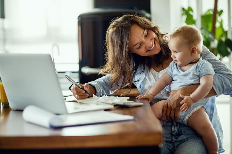 A working mother happily holding her baby, and working remotely